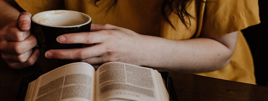 mulher desenvolvendo hábitos de leitura lendo um livro com uma xícara de café nas mãos